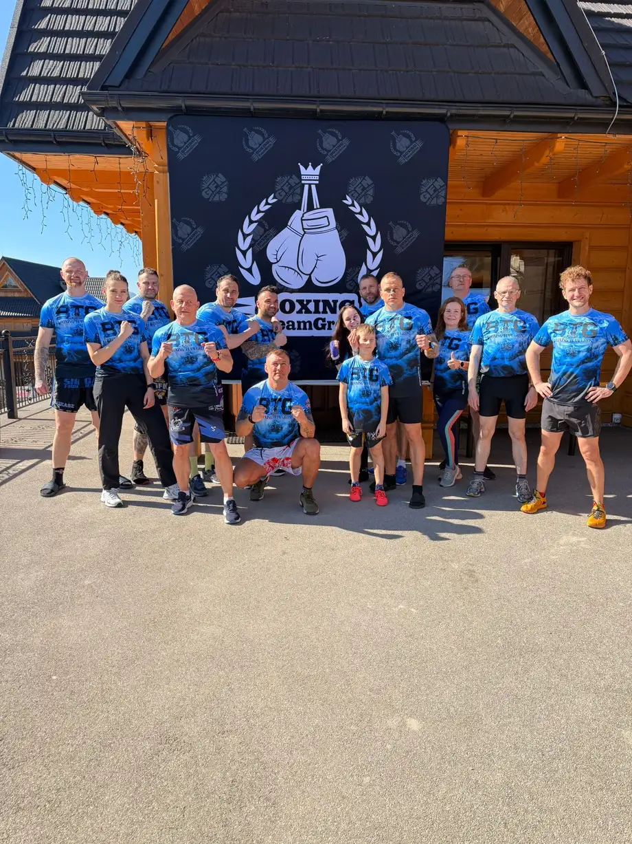 Grupa klubu w koszulkach BTG pod banerem przed góralską chatą